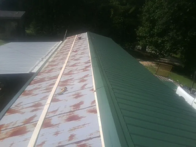 Old rusted panels beside newly installed green metal roofing — Wind Damage Roof Repair by Roofing Brothers in Lowell